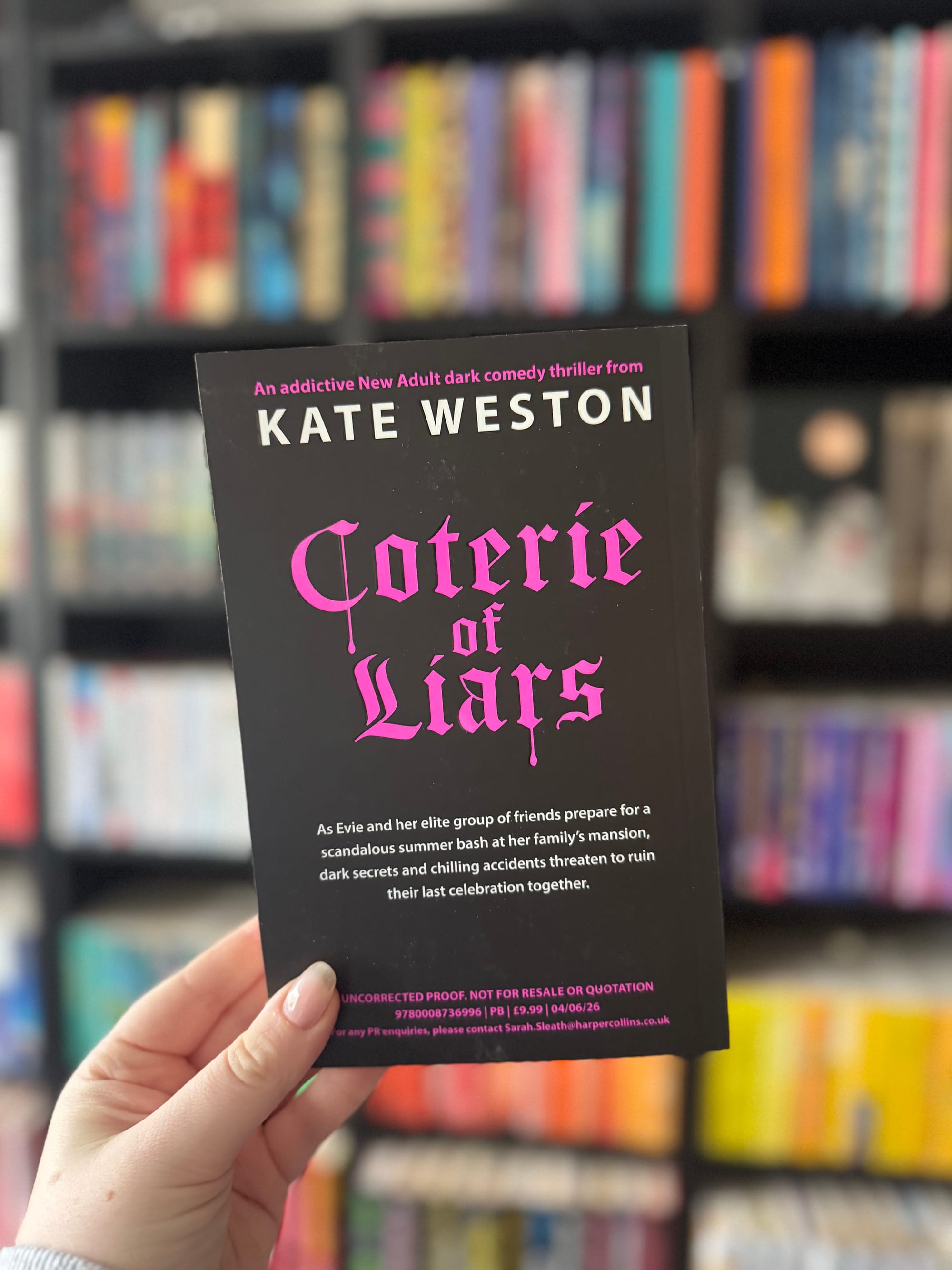 The back of a black proof copy booklet held in a hand, with bold pink gothic lettering reading “Coterie of Liars” by Kate Weston. Smaller text describes it as a dark comedy thriller, with a brief plot teaser below.