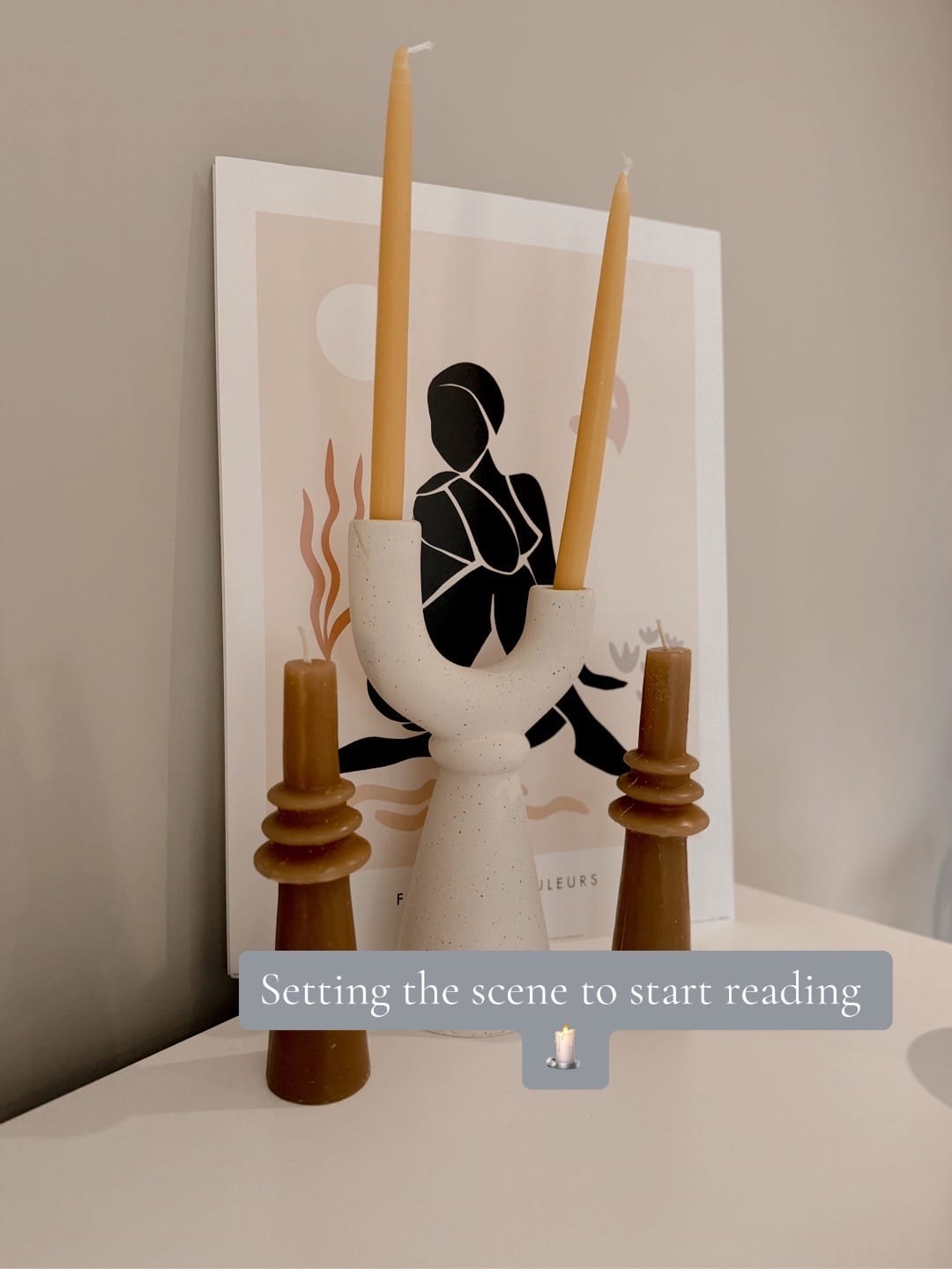 Two tall yellow candles in a white holder, framed art silhouette, text reads: Setting the scene to start reading. Cozy ambiance.