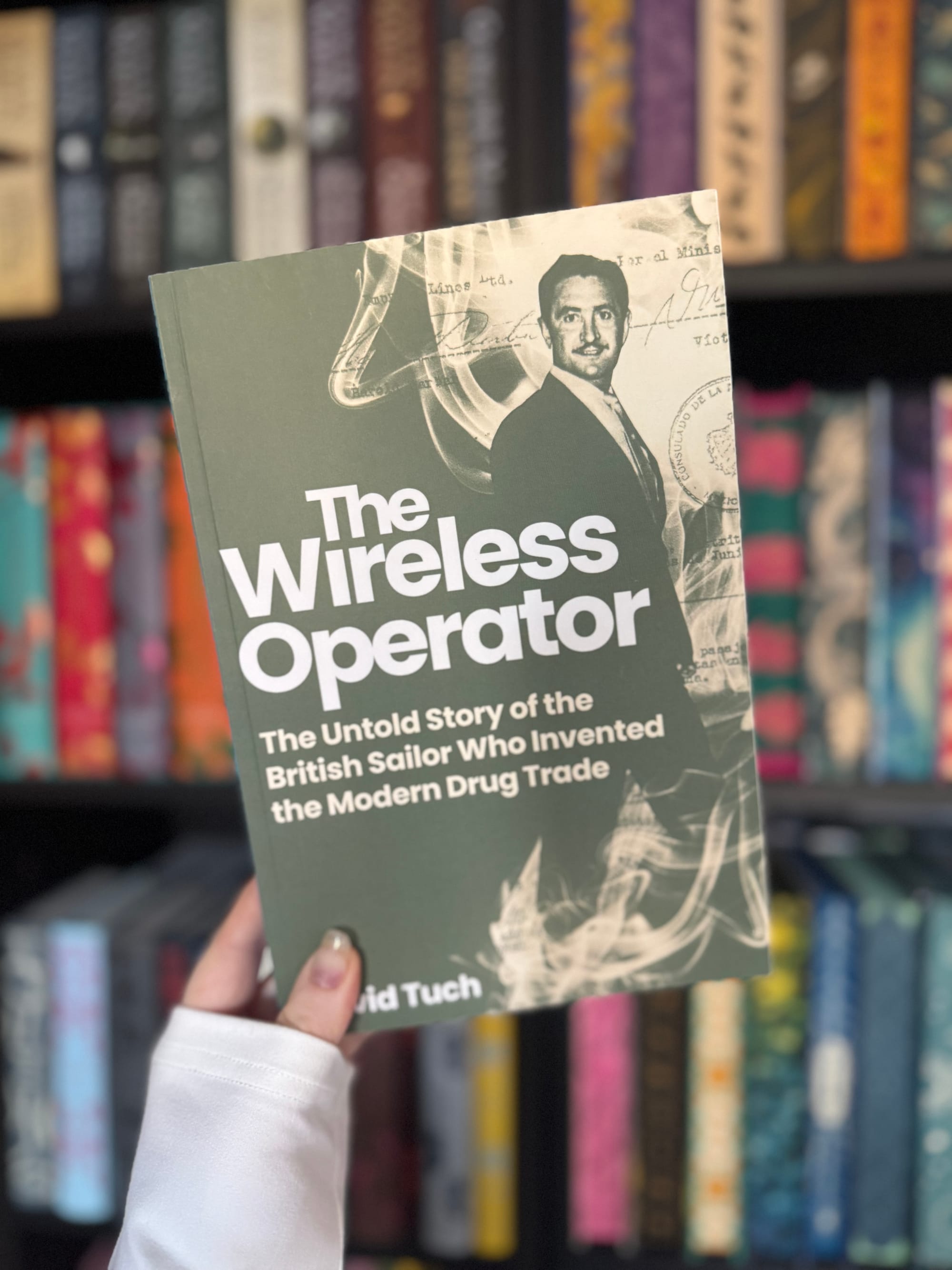 Hand holding a book titled "The Wireless Operator" with a vintage design. Background: colorful books on a shelf, creating a cozy ambiance.