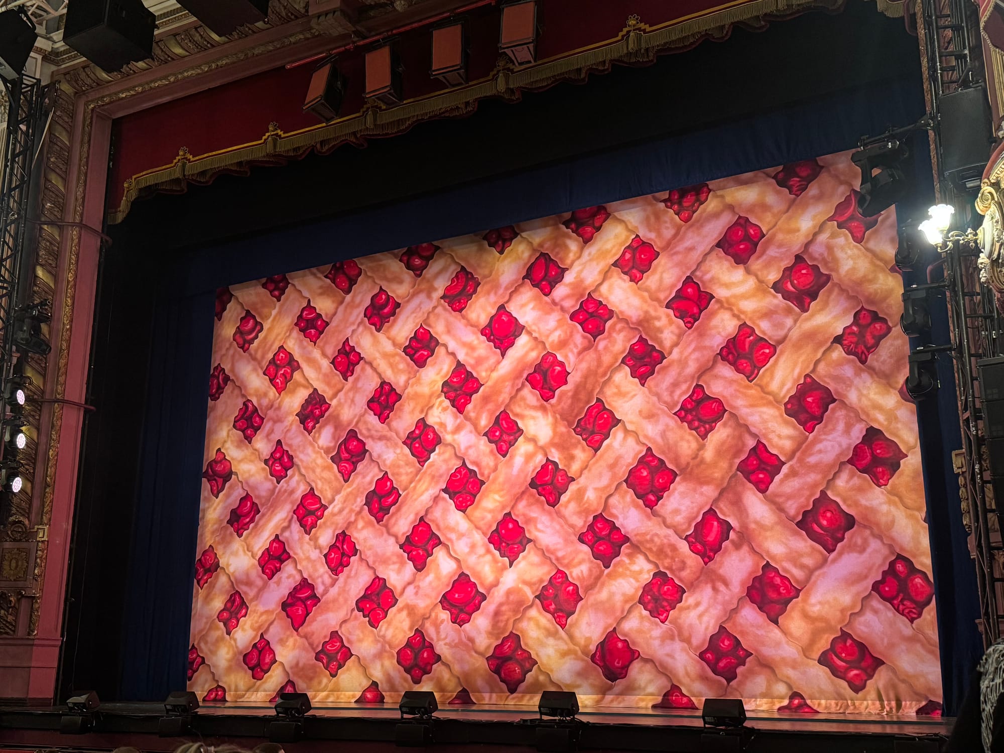 Stage curtain designed like a lattice pie crust with bright red filling, set inside a theatre at Waitress the Musical