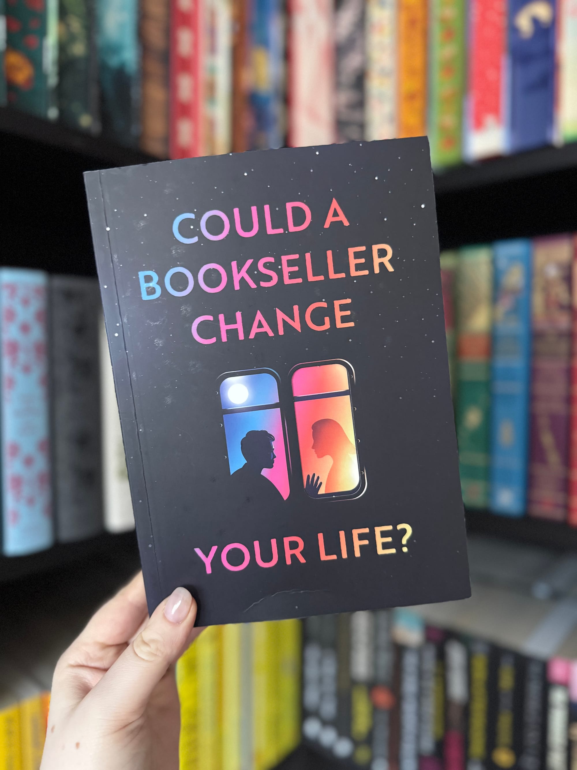 Book cover with silhouette of two people by a window, colorful gradient text saying "Could a Bookseller Change Your Life?" on a bookshelf.