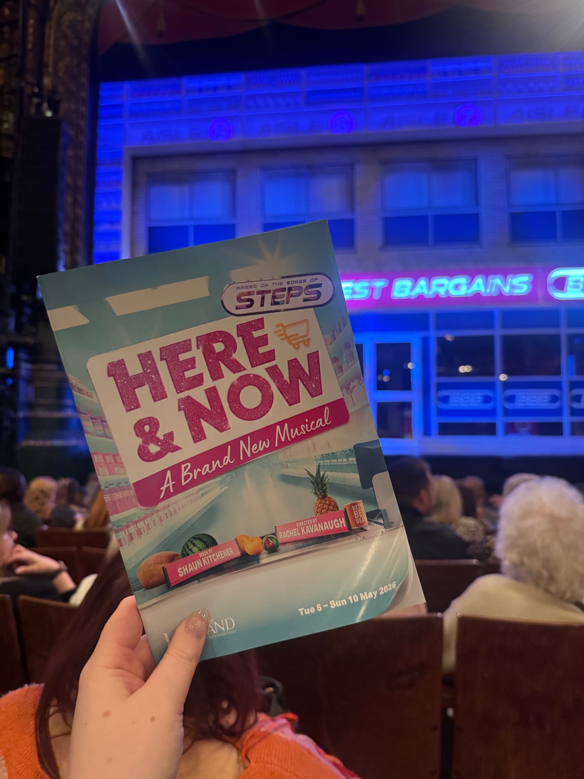 Audience holds a "Here & Now" musical program in a theater with a blue-lit stage, showing excitement. Text: "Based on the songs of Steps."