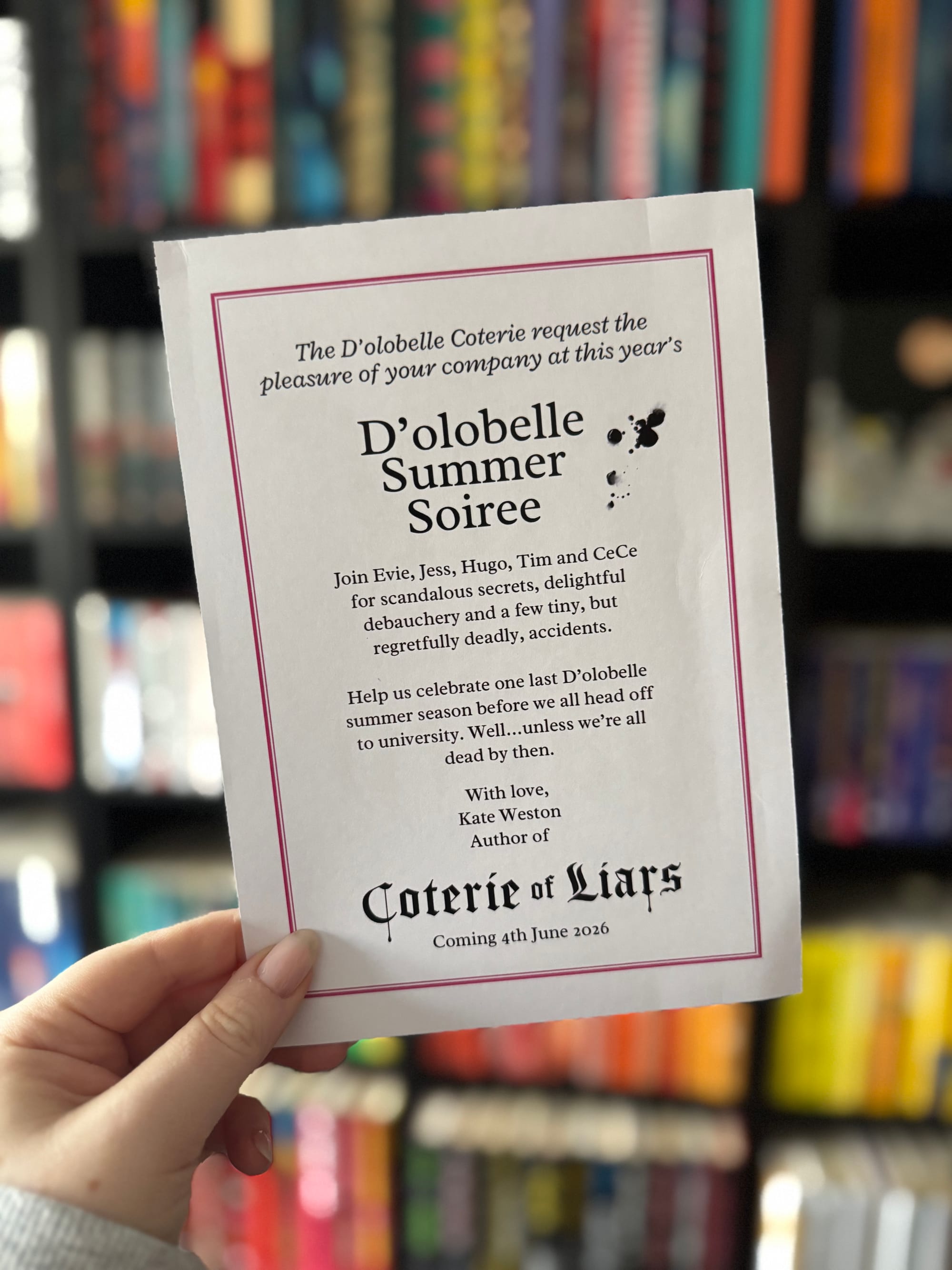 A hand holds the reverse of a printed invitation card bordered in pink. The text invites guests to the “D’olobelle Summer Soiree,” mentioning characters Evie, Jess, Hugo, Tim and CeCe, with a playful but ominous tone about deadly accidents.
