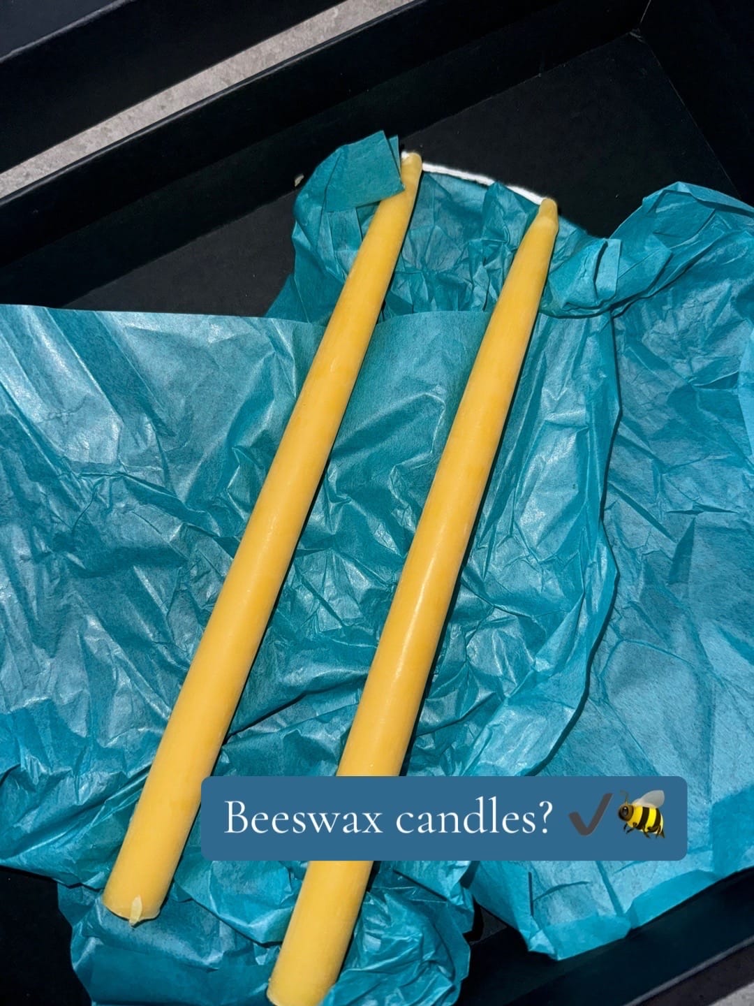 Yellow beeswax candles on teal tissue paper in a black box. Text reads "Beeswax candles?" with checkmark and bee emoji, suggesting approval.