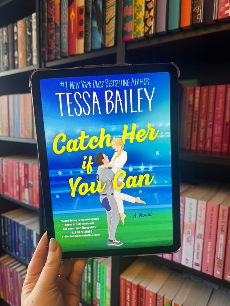 Tablet displaying "Catch Her if You Can" by Tessa Bailey against a colorful bookshelf. A hand holds the device, vibrant book spines visible.