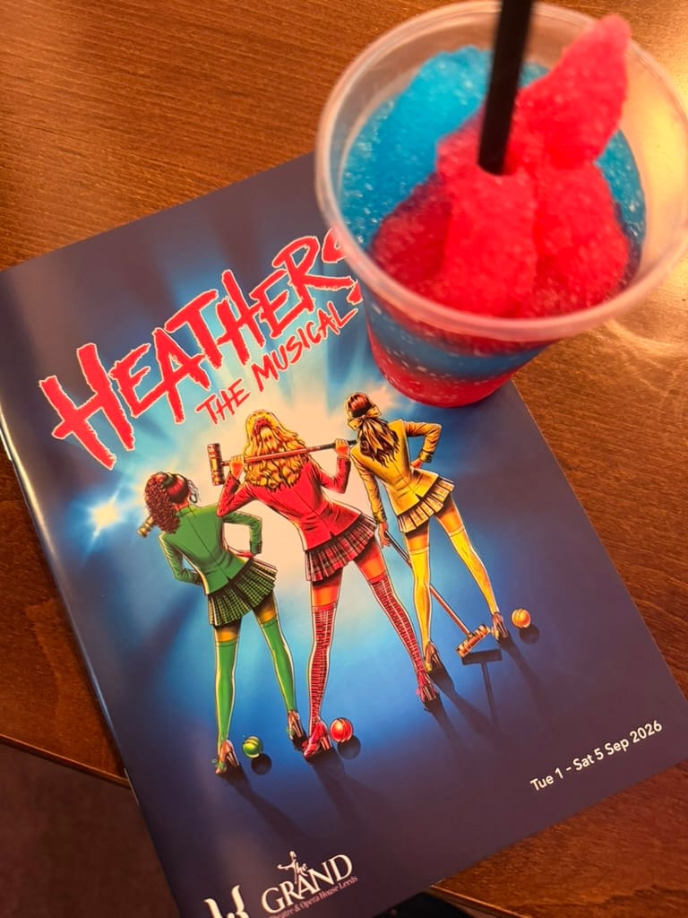 Heathers the Musical programme at Leeds Grand Theatre alongside a red and blue frozen drink.