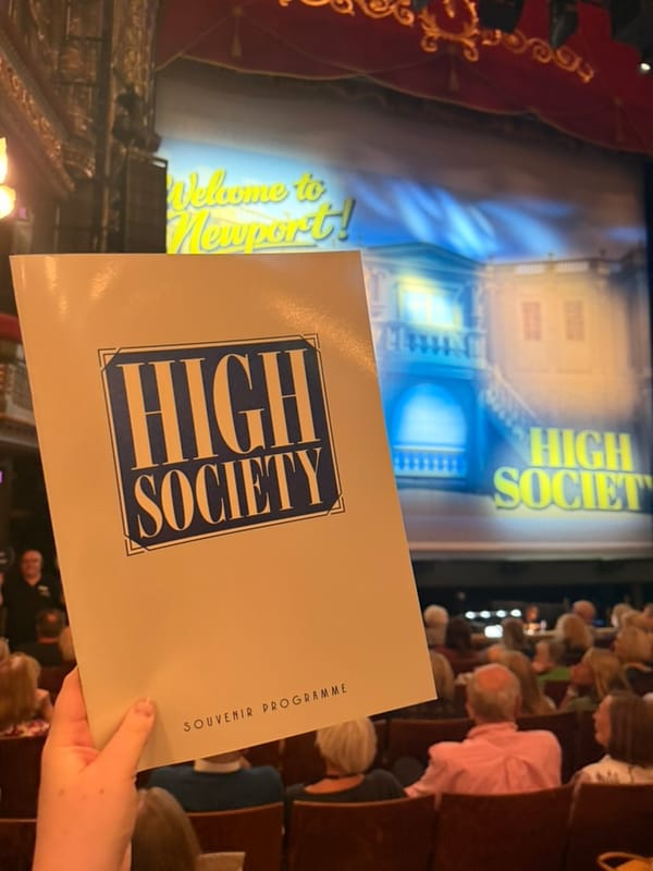 A High Society souvenir programme held up inside a theatre, with the stage in the background