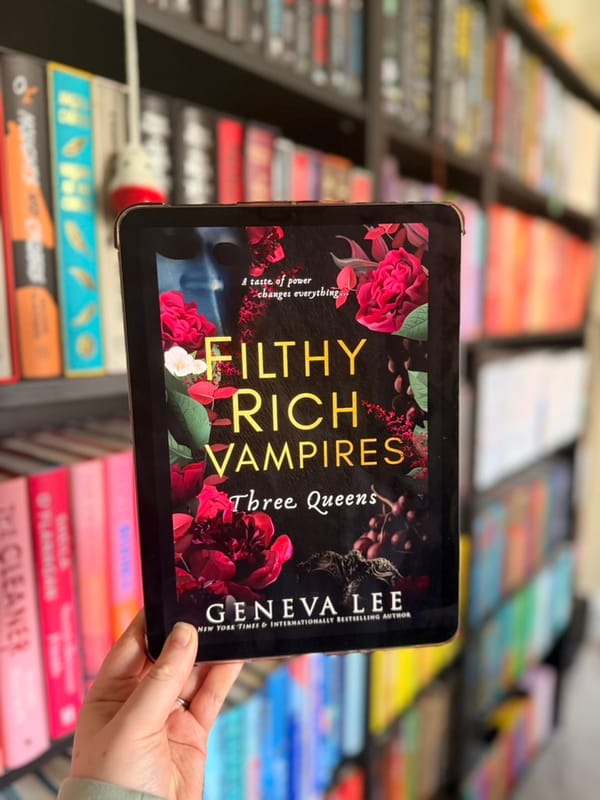 A hand holds a tablet displaying the cover of Three Queens from Geneva Lee’s Filthy Rich Vampires series.